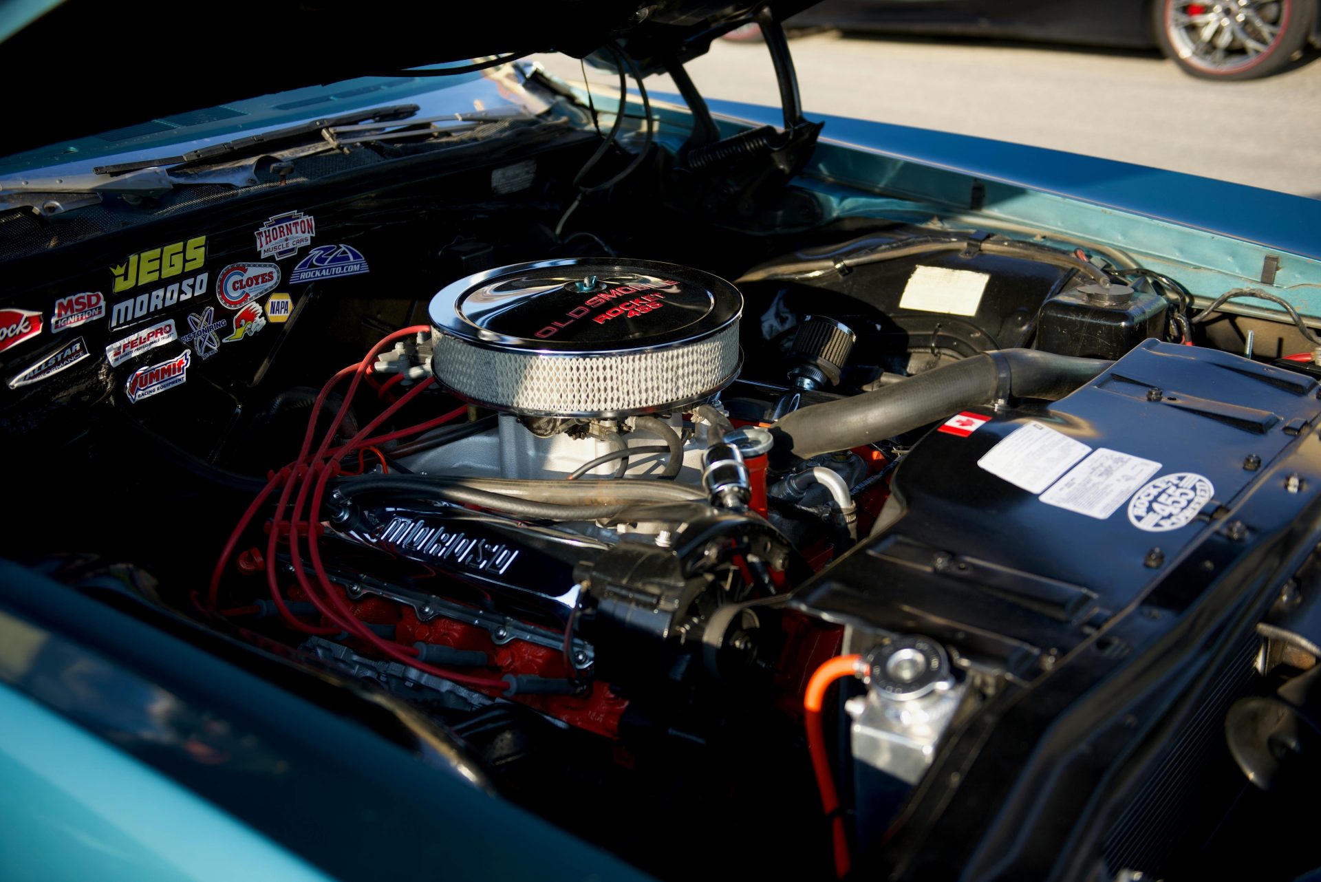 Detailansicht eines Oldtimermotors mit Tuningteilen und verschiedenen Markenaufklebern.